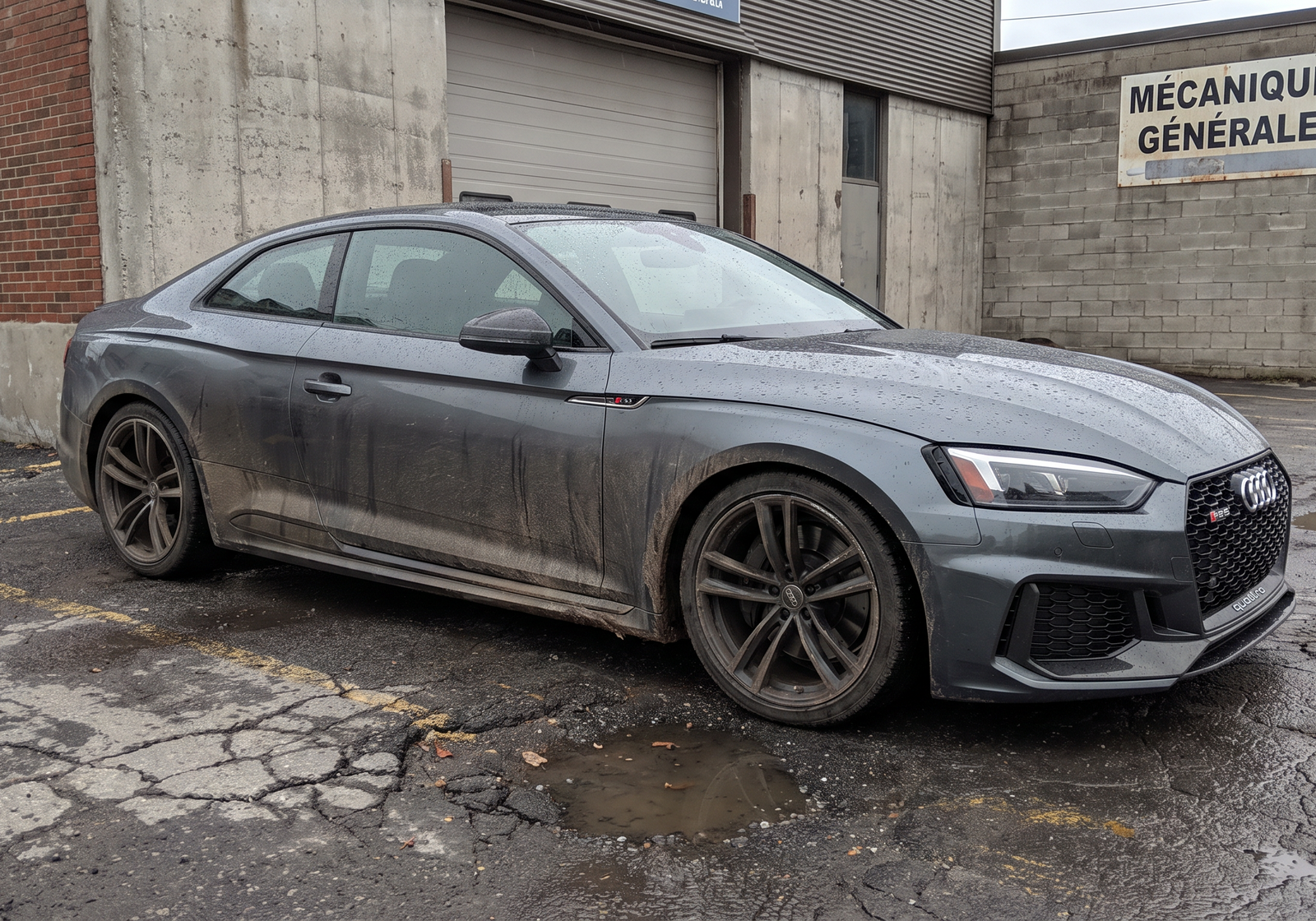 Illustration: dirty dark Audi RS5 coupe parked outside a wet workshop on an overcast day
