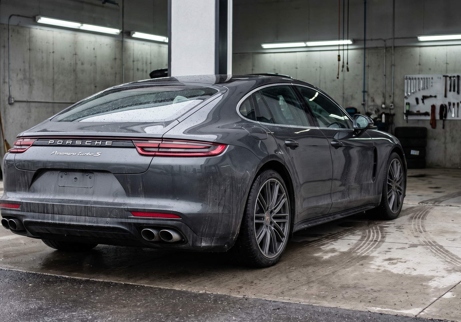 Illustration of a grey Porsche Panamera Turbo S-style sedan outside a wet workshop, with rear exhaust tips visible.