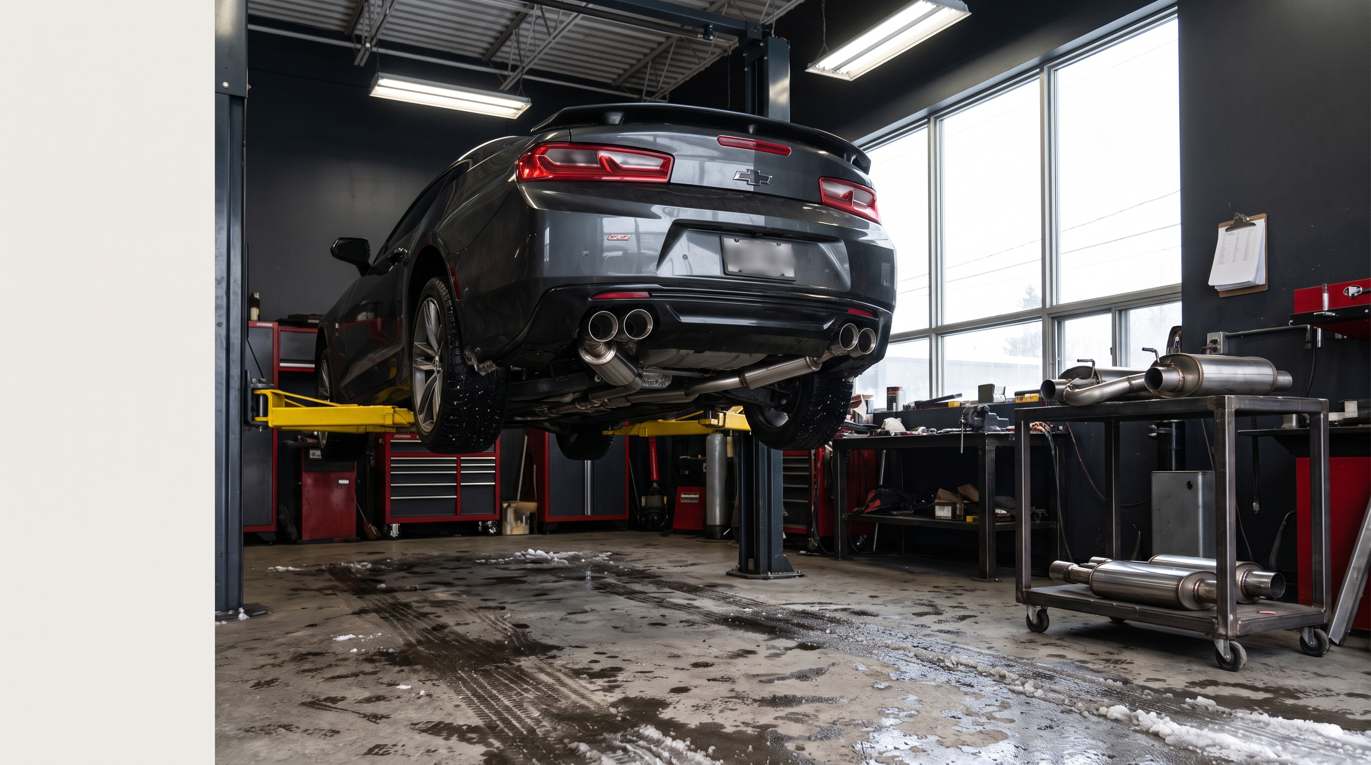 Performance coupe on a lift in a Quebec exhaust workshop with muffler and catback components staged for inspection