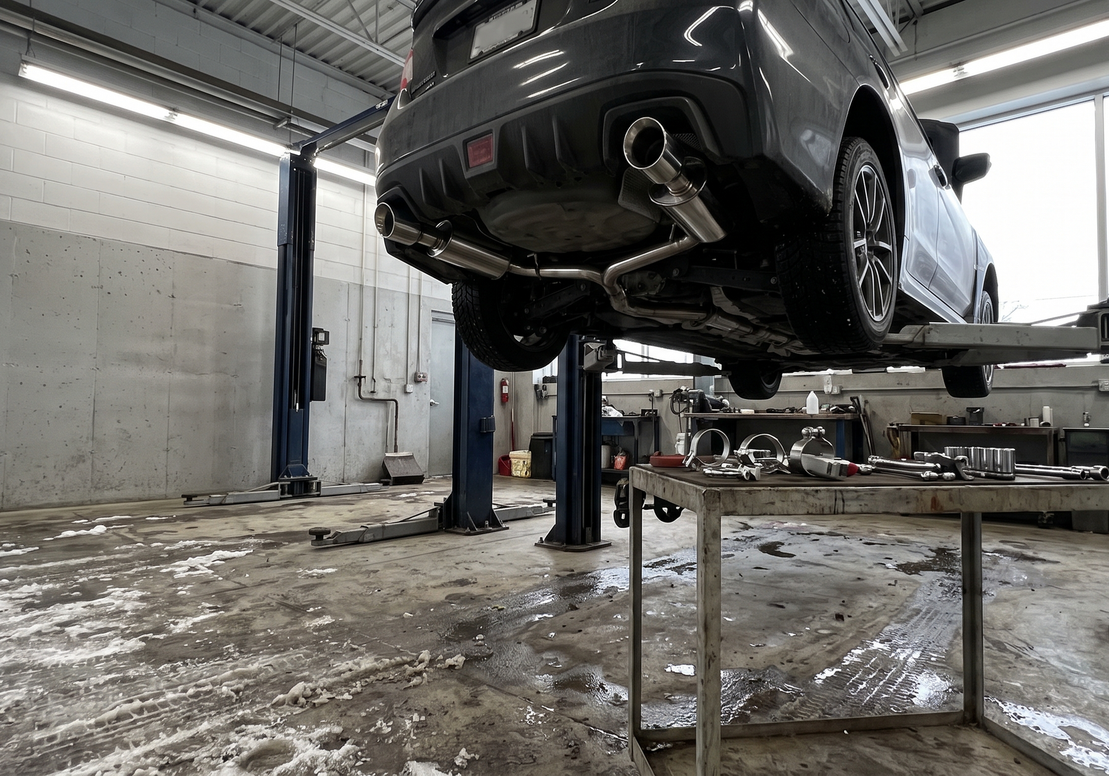 Performance exhaust workshop with a coupe on a lift and exhaust components for a Montreal and Brossard shop checklist
